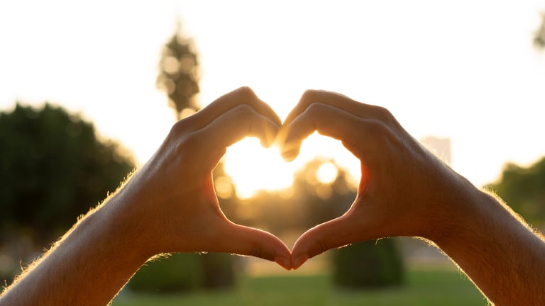 Manos formando corazón al atardecer con fondo cálido